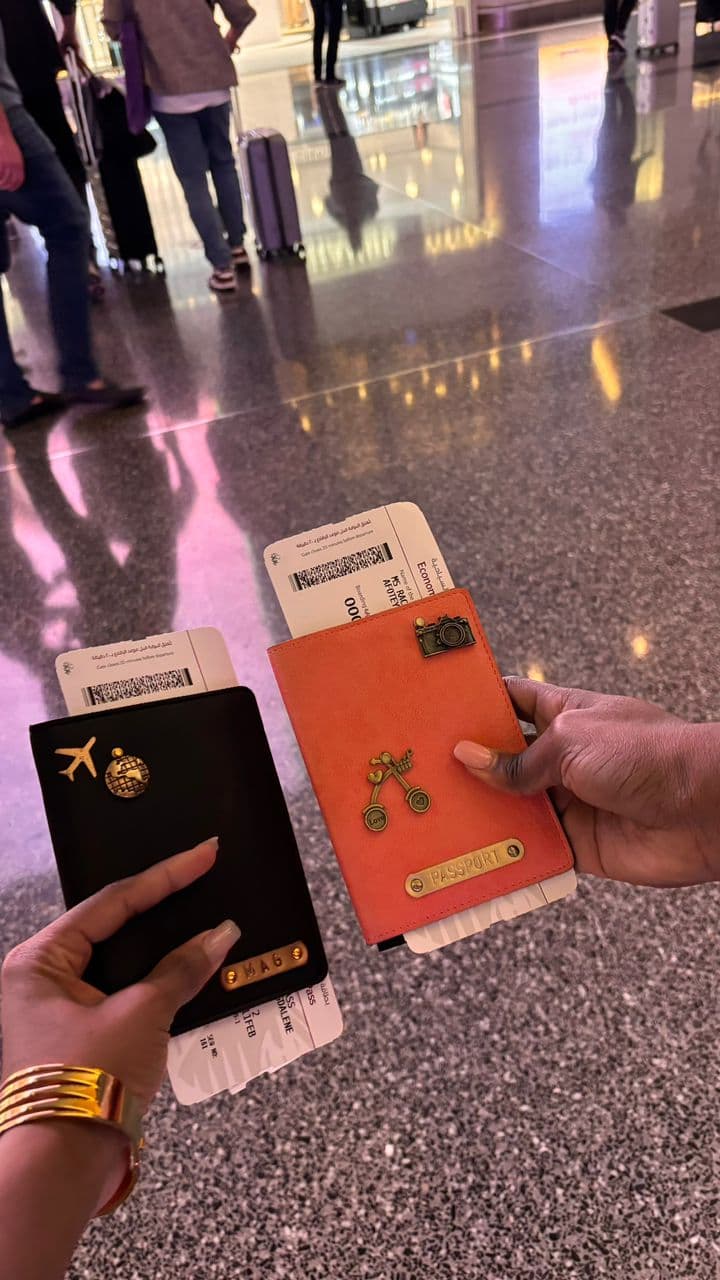 Two personalised passport covers with gold charms and leather name strips held at the airport with boarding passes
