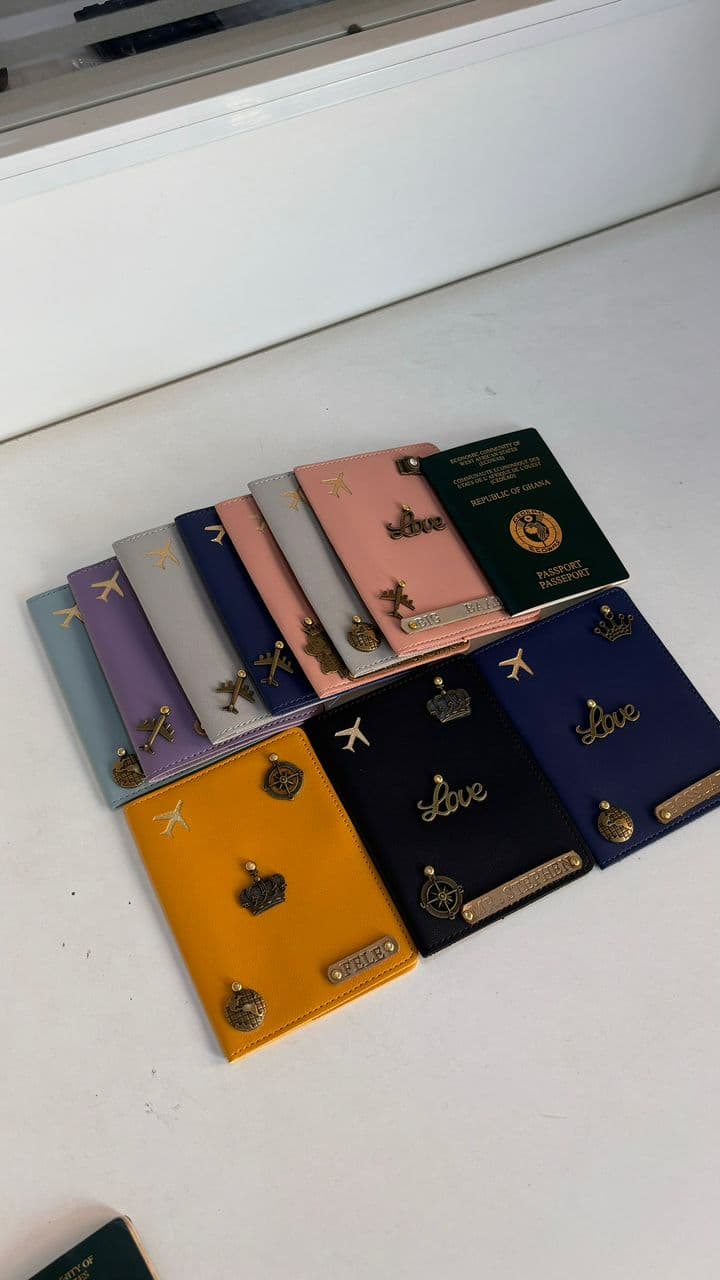 A collection of personalised P.U leather passport covers in many colours with gold charms and name strips beside a Republic of Ghana passport