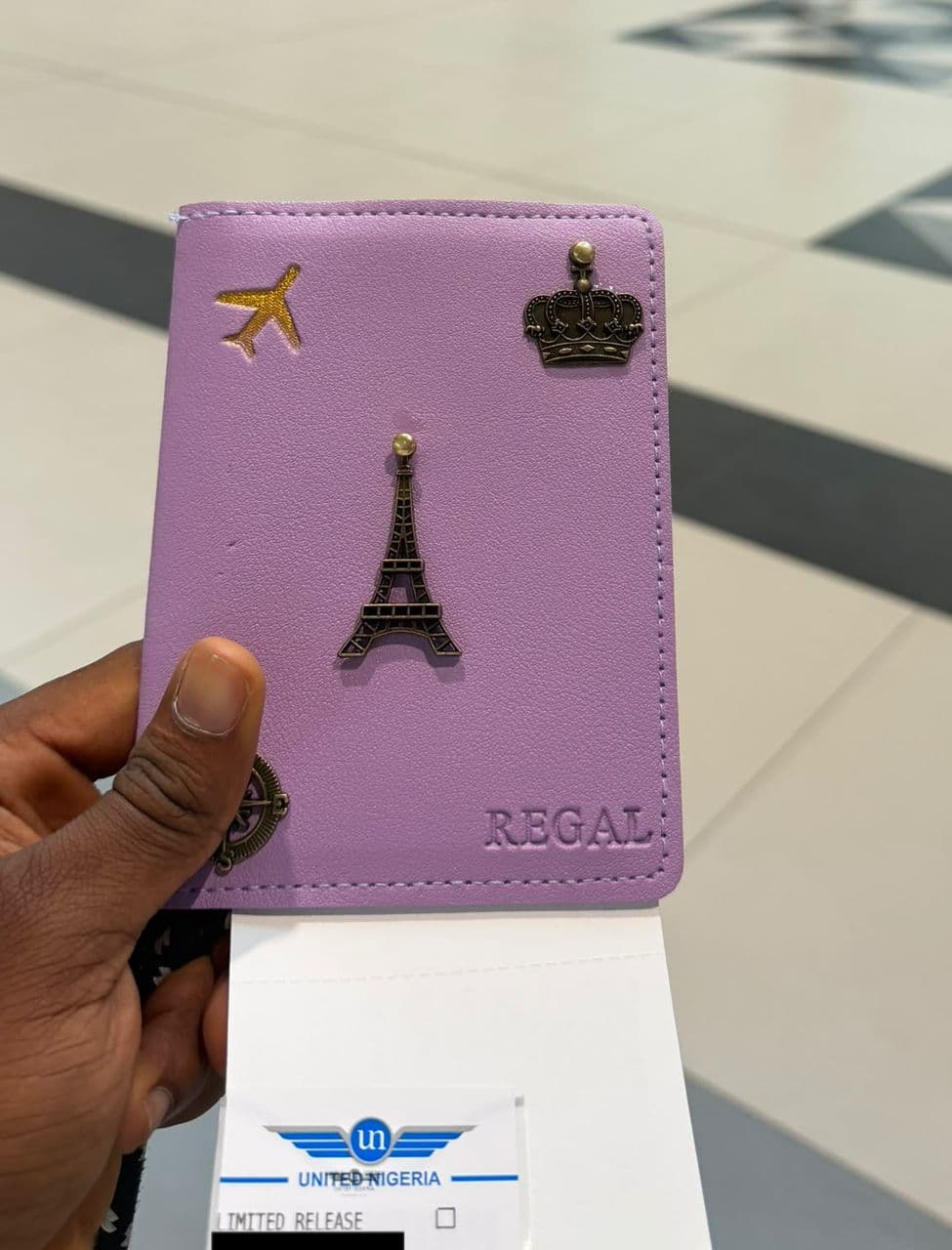 Personalised purple passport cover with gold charms, embossed REGAL, held at the airport